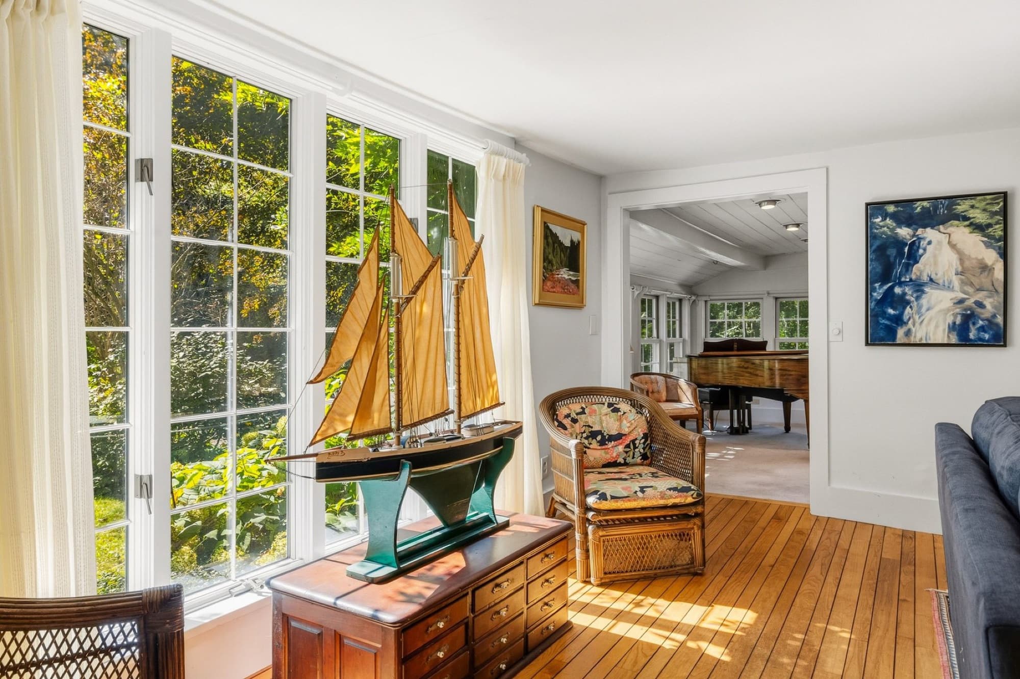 The living room's wall of windows with a model sailboat, looking into the sunroom