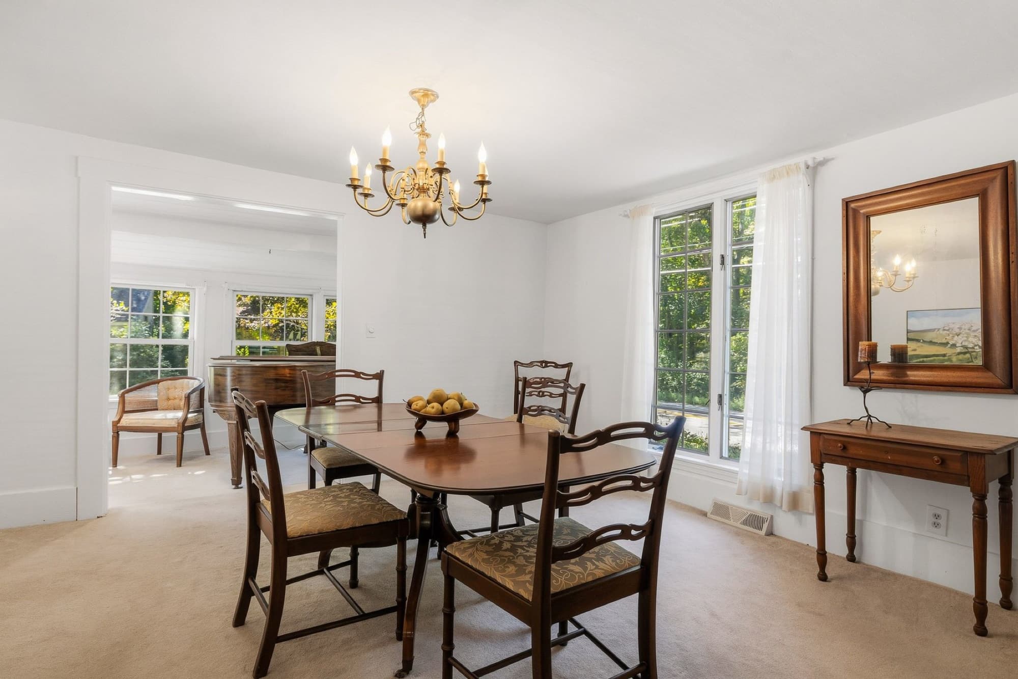 The dining room with a chandelier and a mirror, open to the sunroom