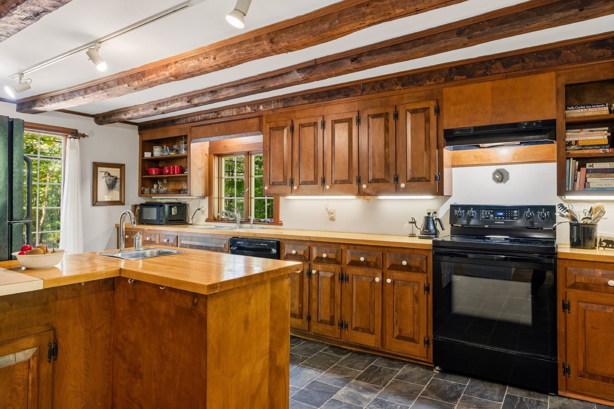 The kitchen with exposed beams, wood cabinets, a butcher block island, and a gray tile floor