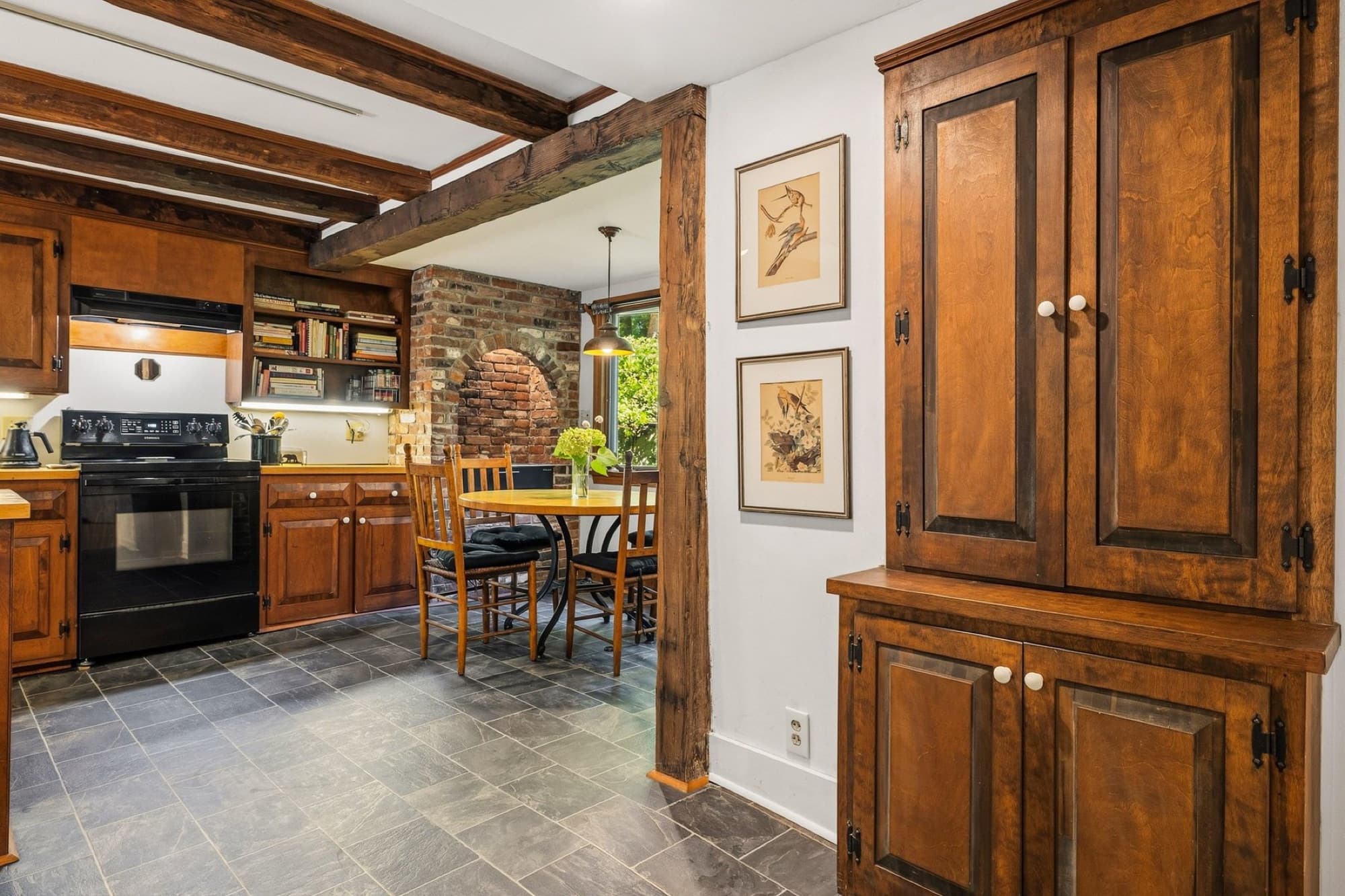 The kitchen's exposed beams and a tall wood cupboard, looking toward the range