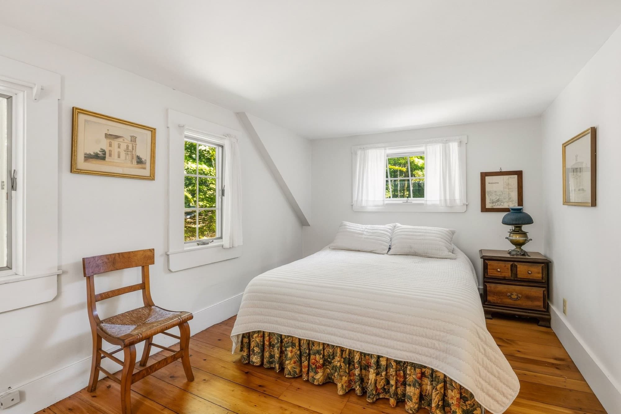 A bedroom under the eaves with wide-plank floors and 2 windows