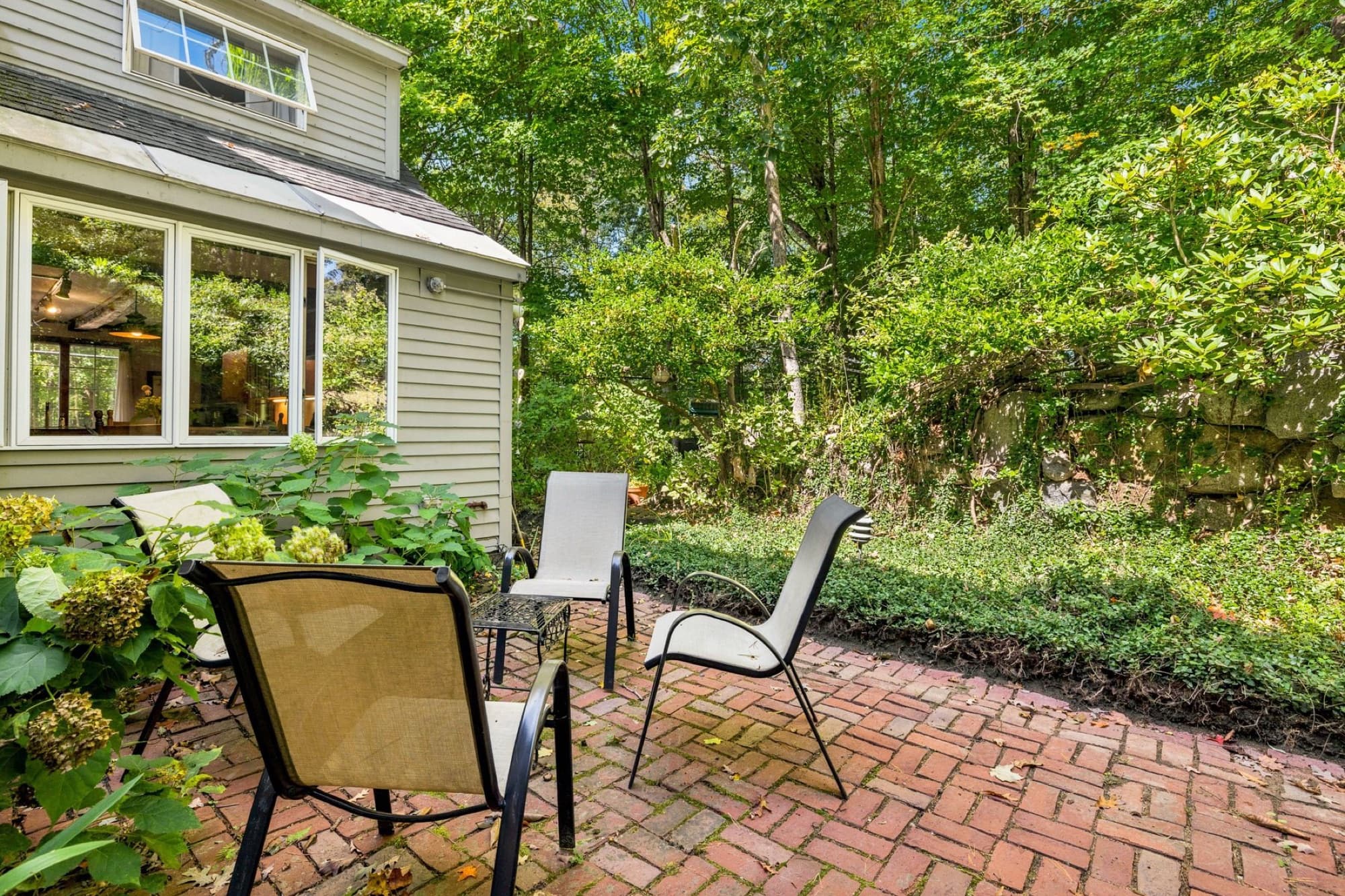 The brick patio behind the house, with chairs beside a stone wall and the sunroom windows