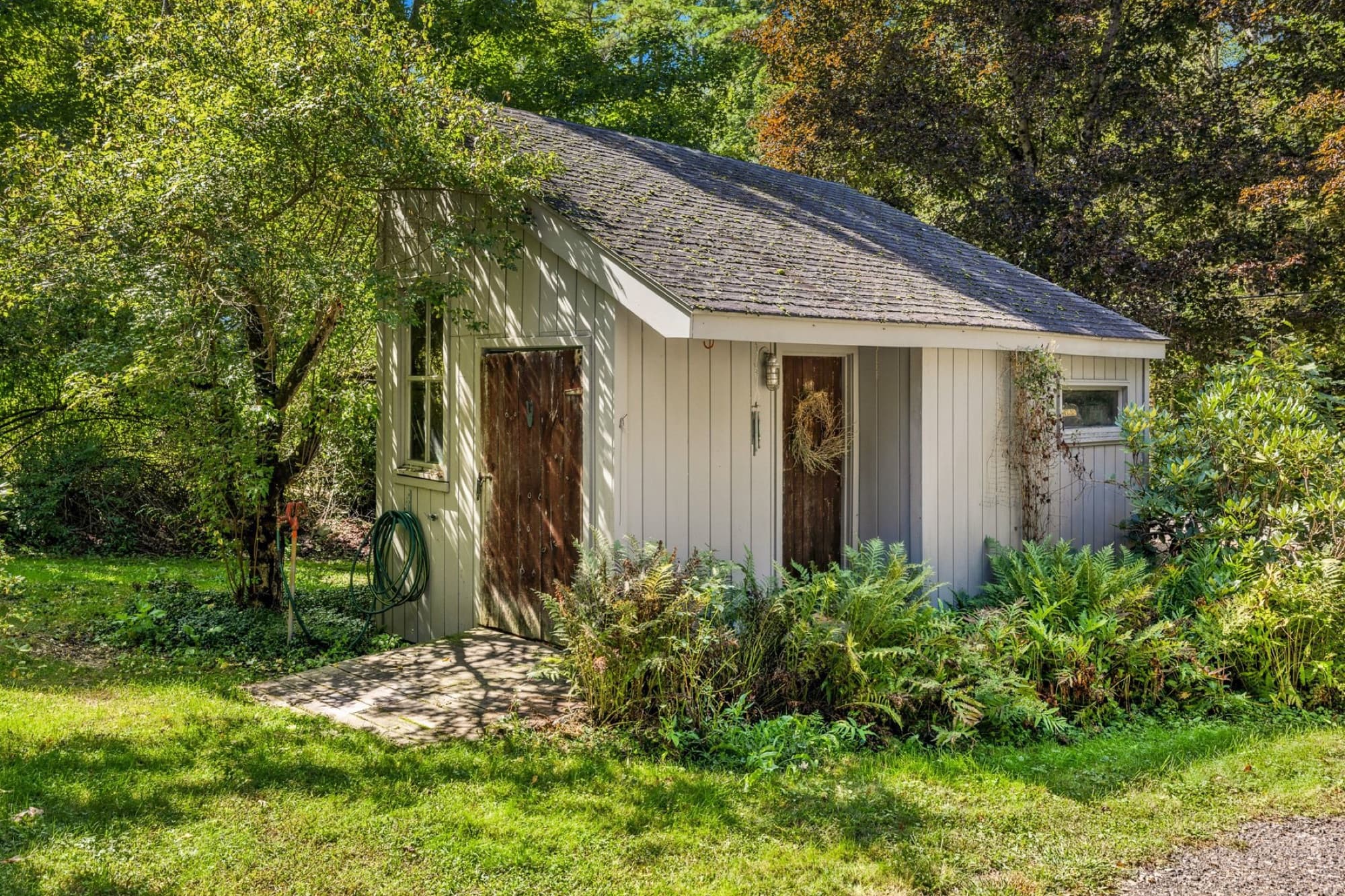 A small gray outbuilding with a door and a window, set in the gardens